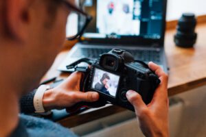 male hands holding professional camera looks photos sitting at cafe with laptop